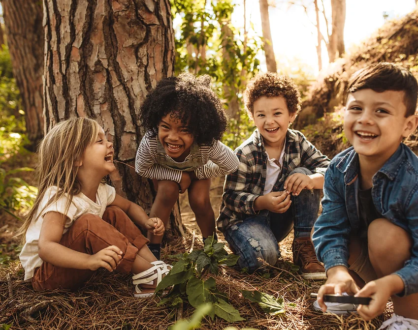 Four children laugh at the foot of a tree.